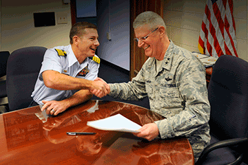 Maj. Gen. Mark E. Bartman, Ohio adjutant general shakes hands with Capt. Greg Rothrock, Coast Guard Research and Development Center commanding officer at table after signing of joint memorandum of understanding.