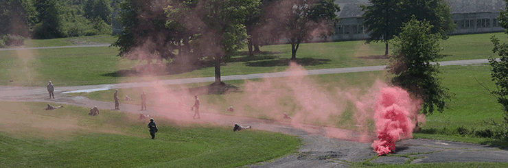 With pink smoke bomb on path in grassy lawn, Soldiers take cover after being ambushed during a foot patrol.