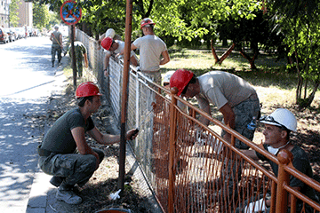 Soldiers painting chain linked fence on school grounds.