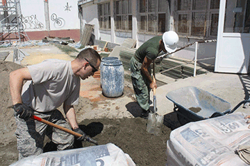 Soldiers mixing concrete outside school.
