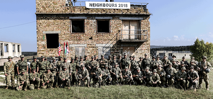Group shot of Soldiers in front of brick building with sign that reads NEIGHBOURS 2018.