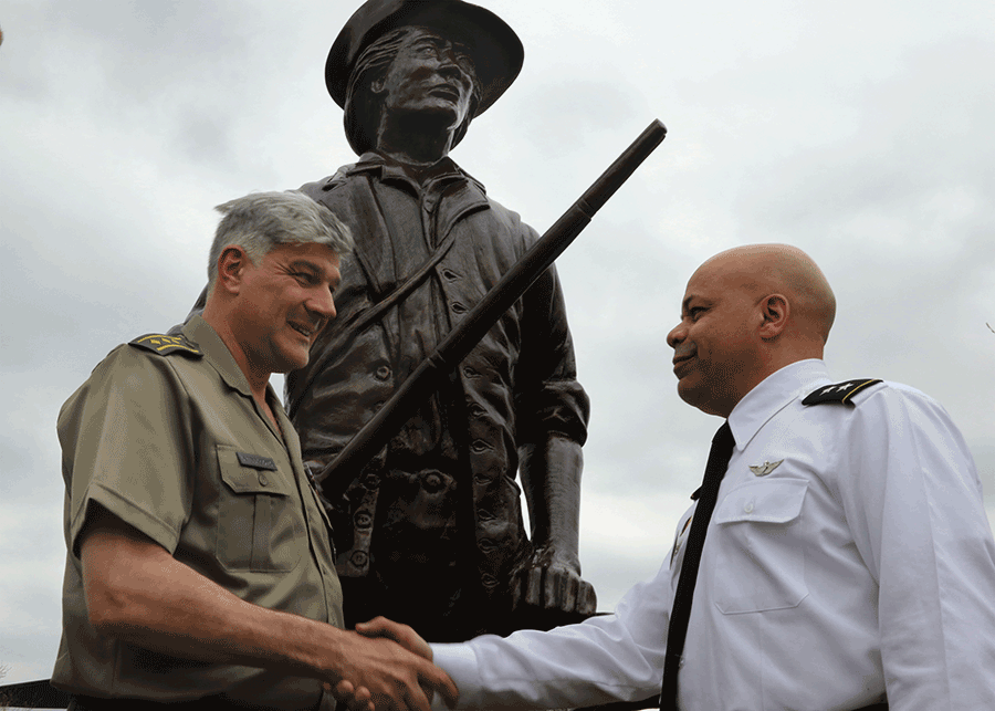 Men shake hands in front of minuteman statue.