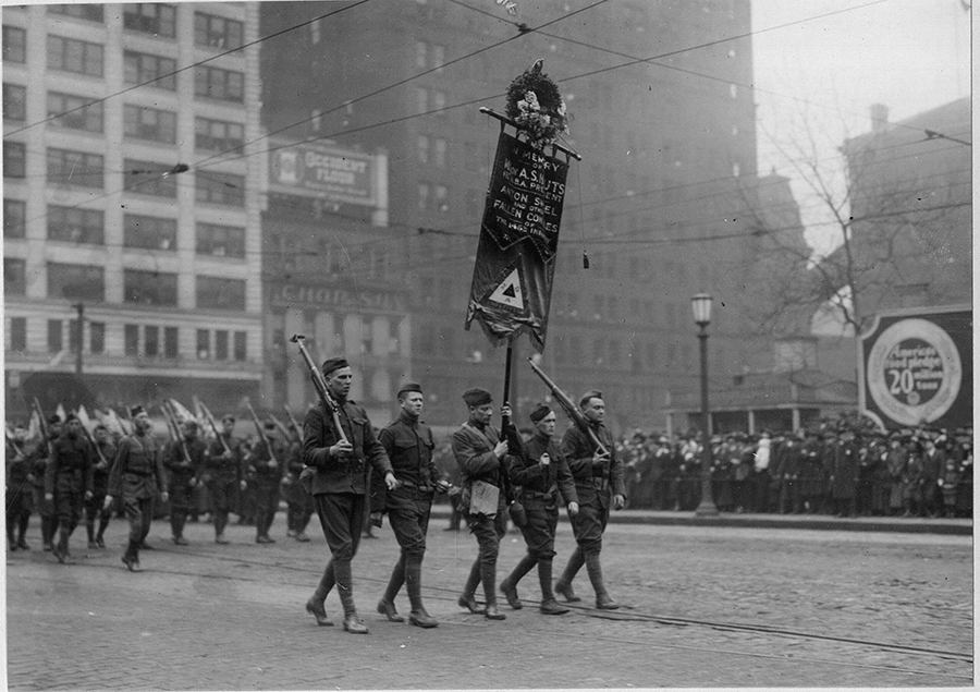 Historic black and white photo of Soldiers carrying banner in parade.