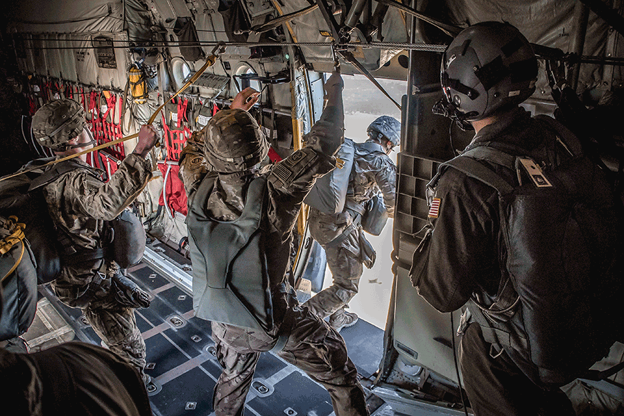 Paratroopers stand inside open door of C-130H Hercules preparing for jump.