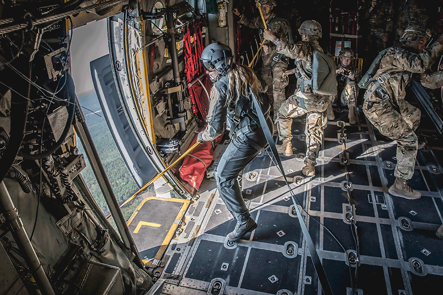 Staff Sgt. Kaitlyn Mueller holds line inside open door of C-130H Herlcules in flight.