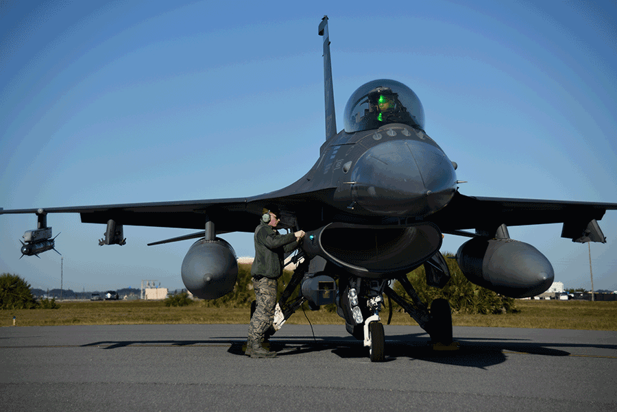 Crew chief stands under wing of F-16 doing a check.