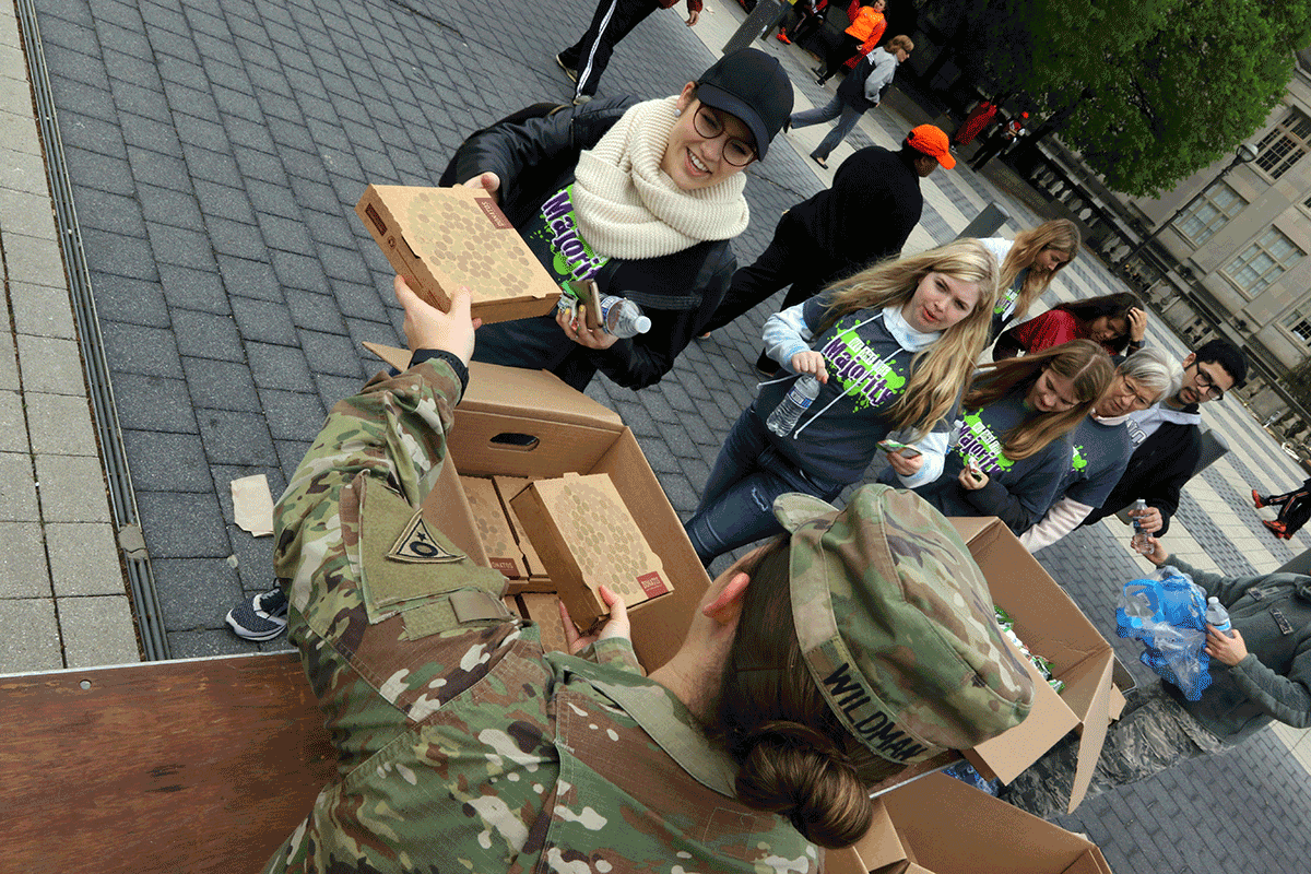 Soldier hands pizza to kids approaching the table.