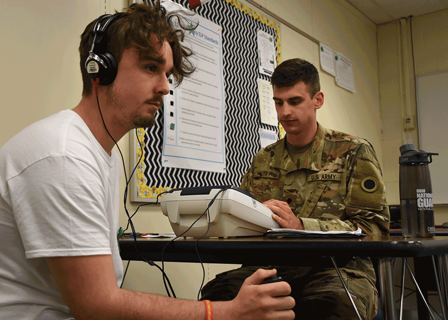 An Ohio Army National Guard health care specialist administers a hearing test to young man using a headset.