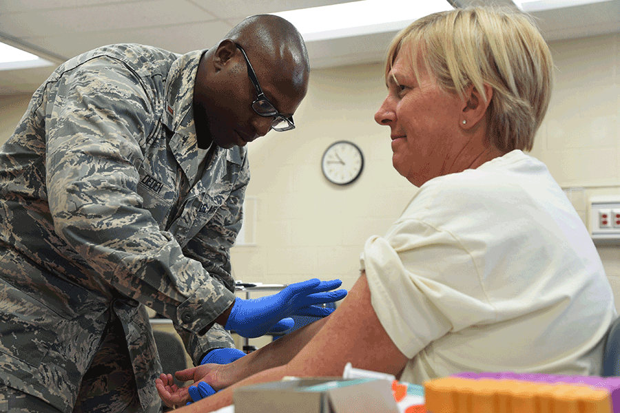 An Airman conducts a blood draw  on woman in chair.