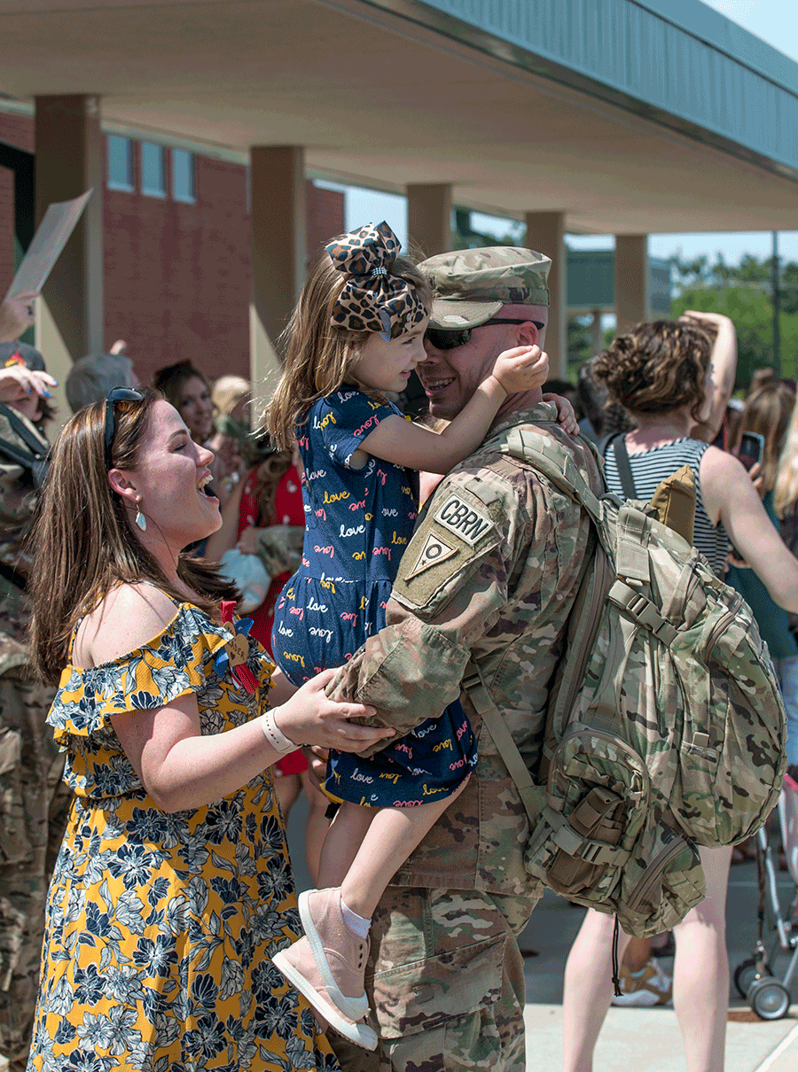 Uniformed Soldier hugs daughters and wife.
