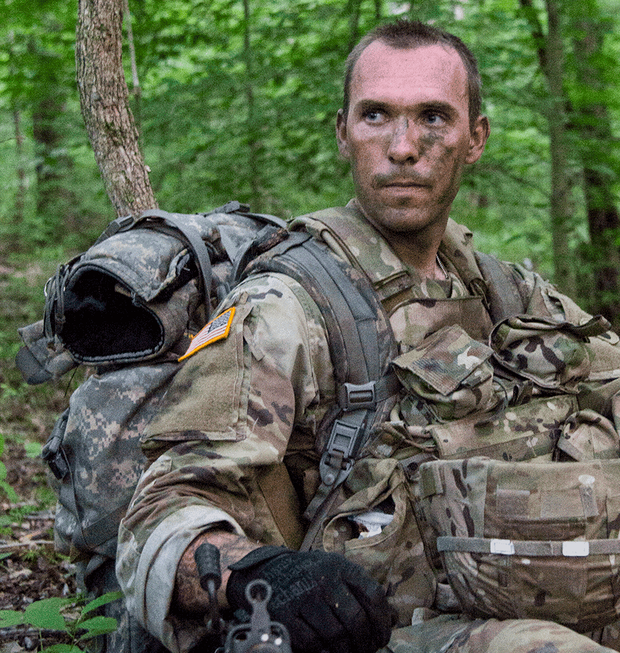 Soldier in camo sitting in field.