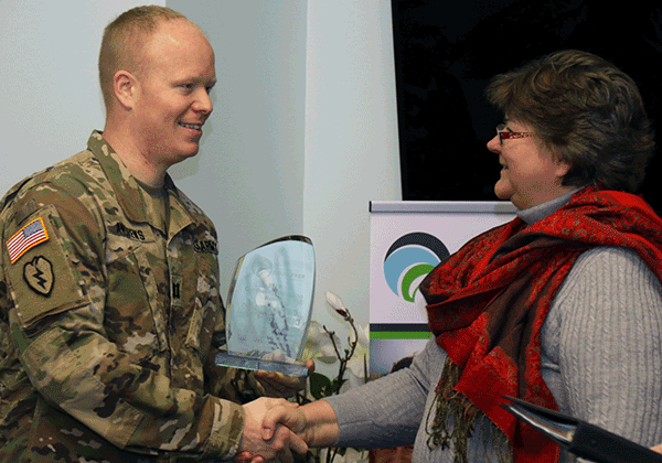 Soldier accepts award while shaking hands.