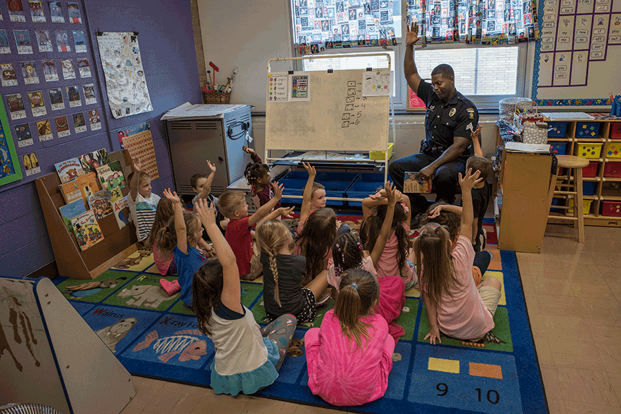 Officer sits at chart in classroom with children on the floor.