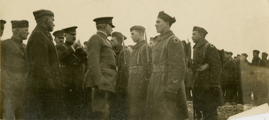 Sepia tone image of Soldiers greeting leaders on snow covered field.