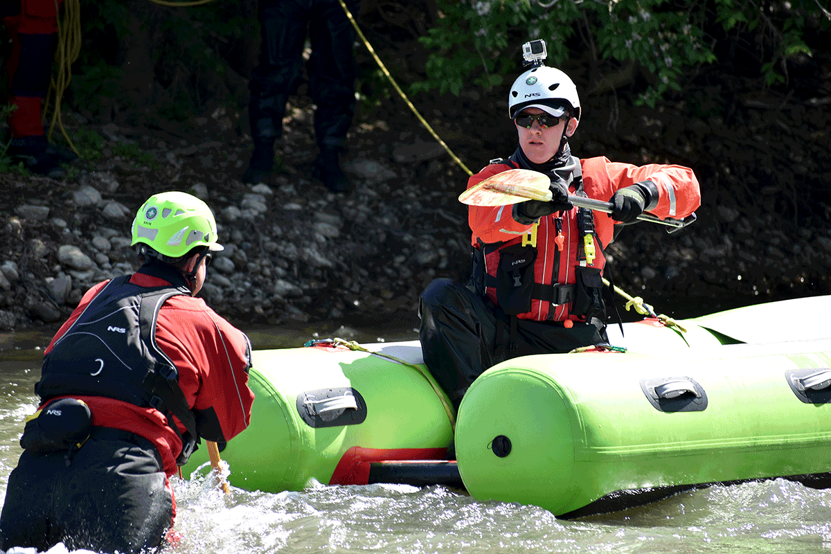 Firefighter approaches person in swift water with raft.