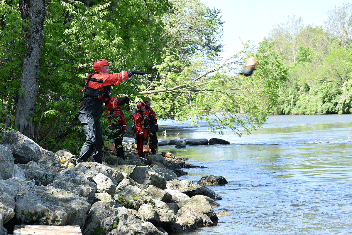 Firefighters on rocky banks of swift river practice tossing throw bags.