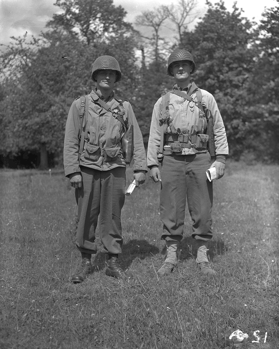 Black and white photo of 2 soldiers standing in field in full gear.