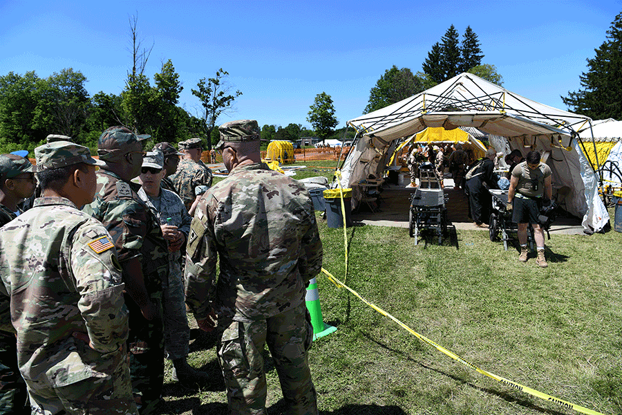 Soldiers gather to observe a tent area housing a decontamination processing line.