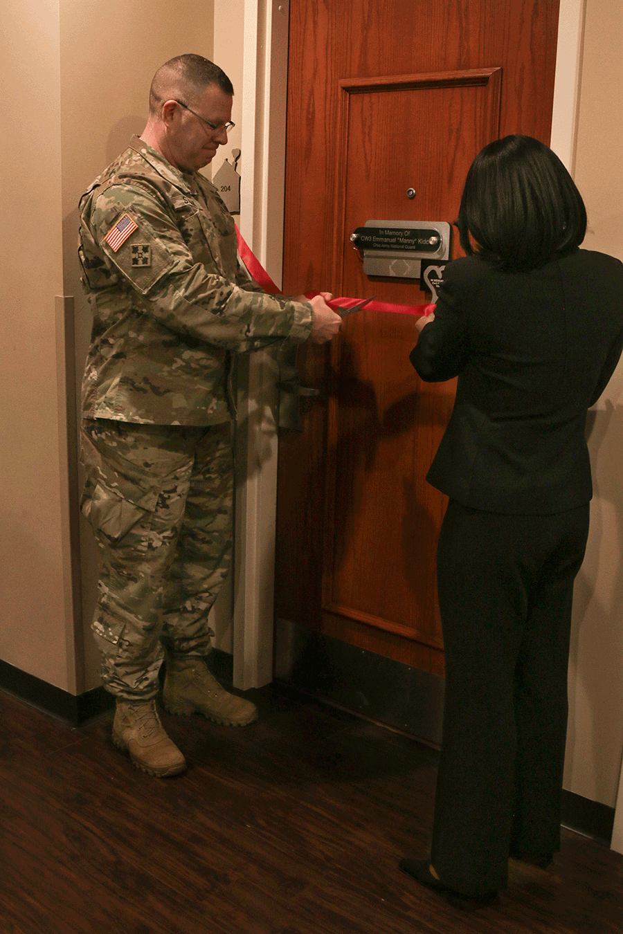 Priscilla Kidd and Col. Daniel Shank cut a red ribbon in front of door to room 204.