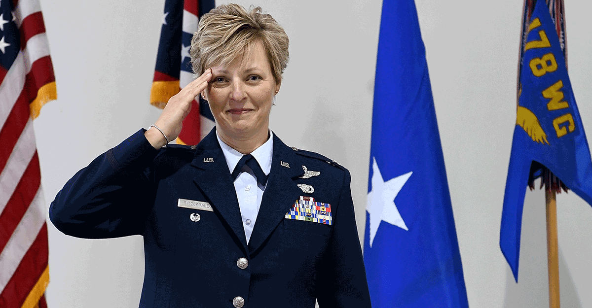 Col. Kimberly A. Fitzgerald salutes in front of the flags.