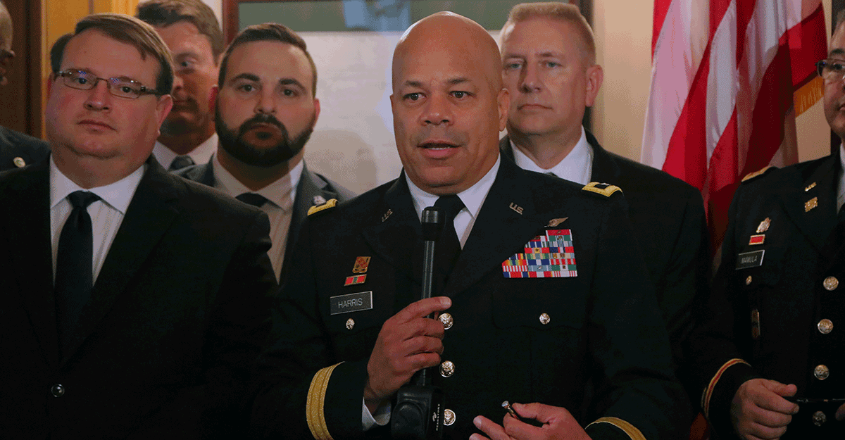 Maj. Gen John C. Harris, Jr. talks at podium with others standing around him.