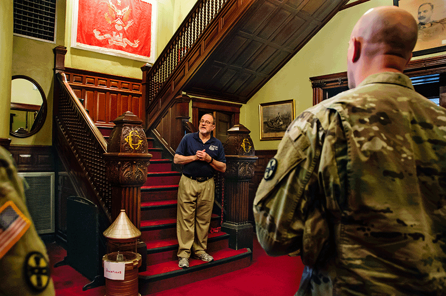 Chairman of the museum committee stands on 1st step of elaborate staircase addressing the Soldiers.
