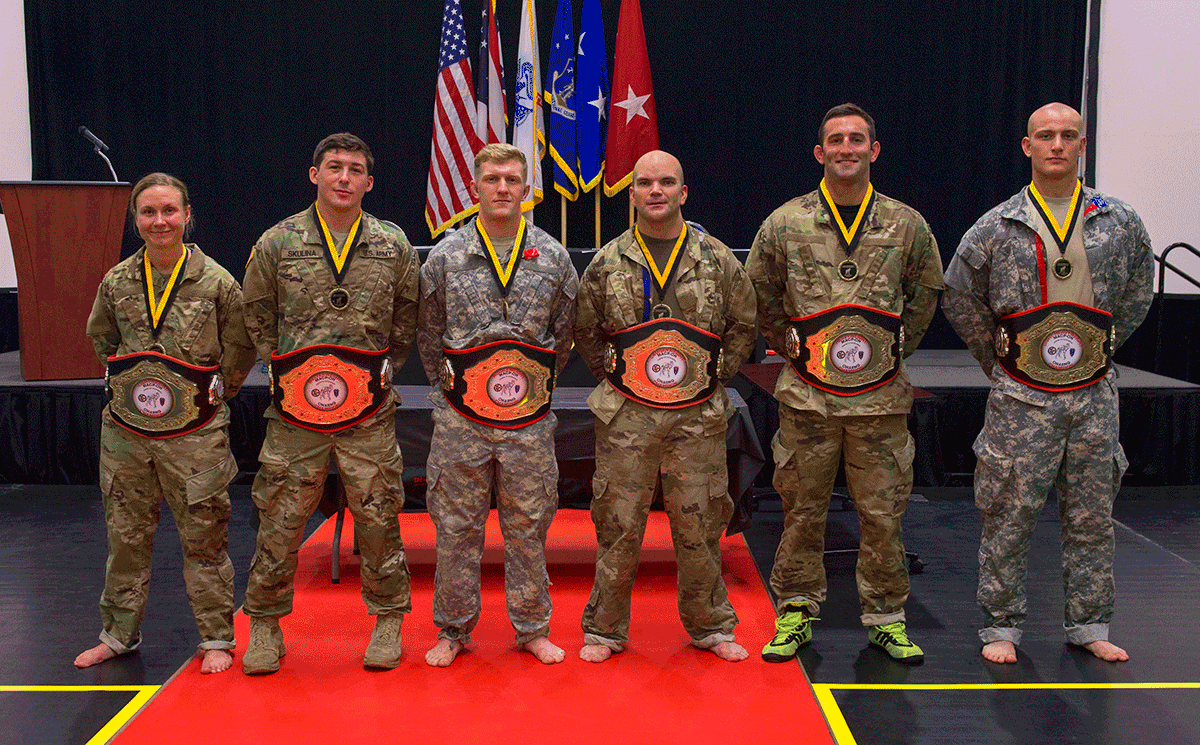 Six Solders stand in row on mat with championship belts on.