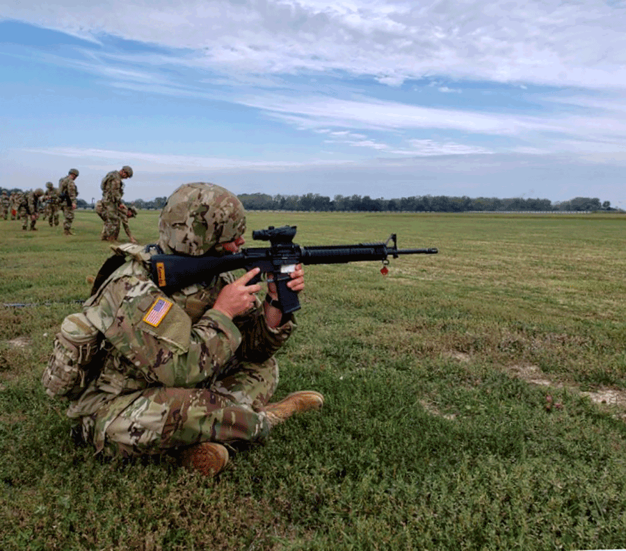 Soldier shoots rifle from aim from a seated position. 