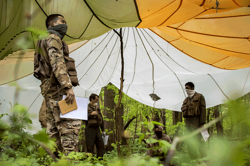 Airmen under large parachute in woods/