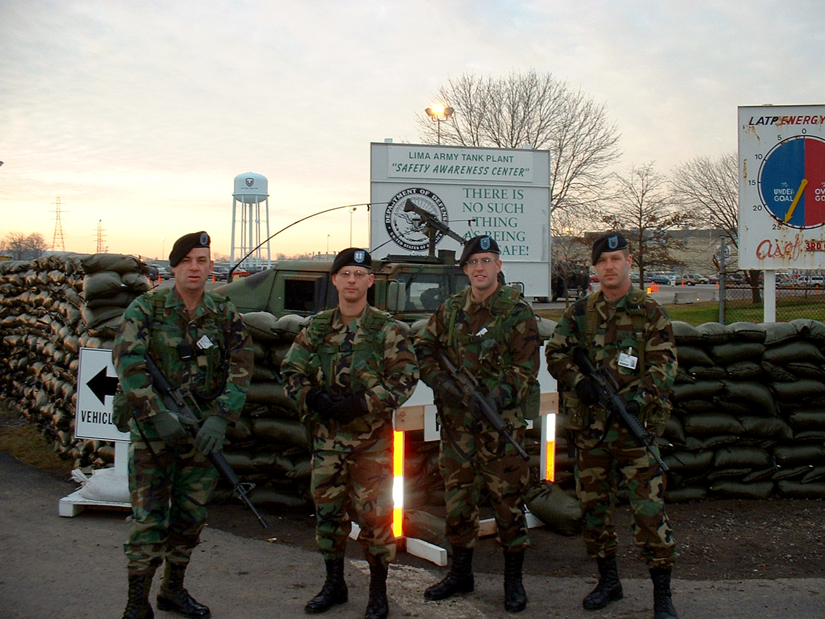 Four Soldiers with rifles pose in front of Lima Army Tank Factory sign.