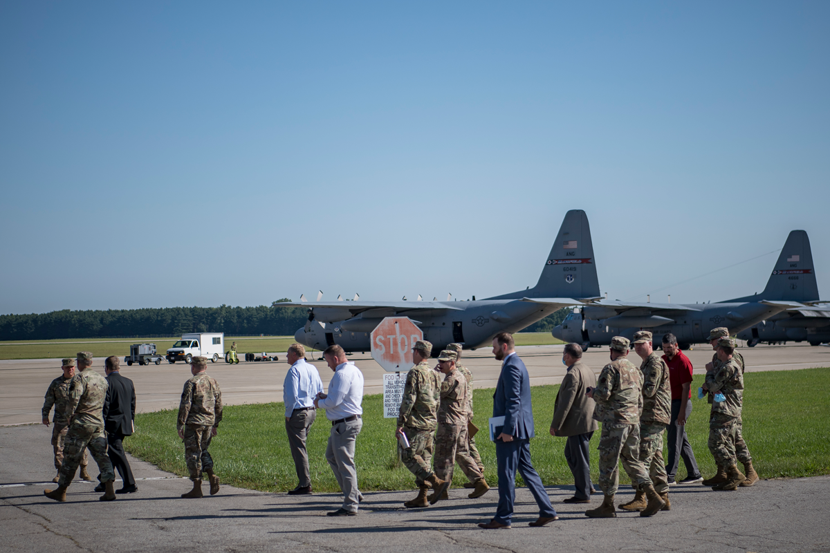 Airmen and civilians walking on base with aircraft in background.
