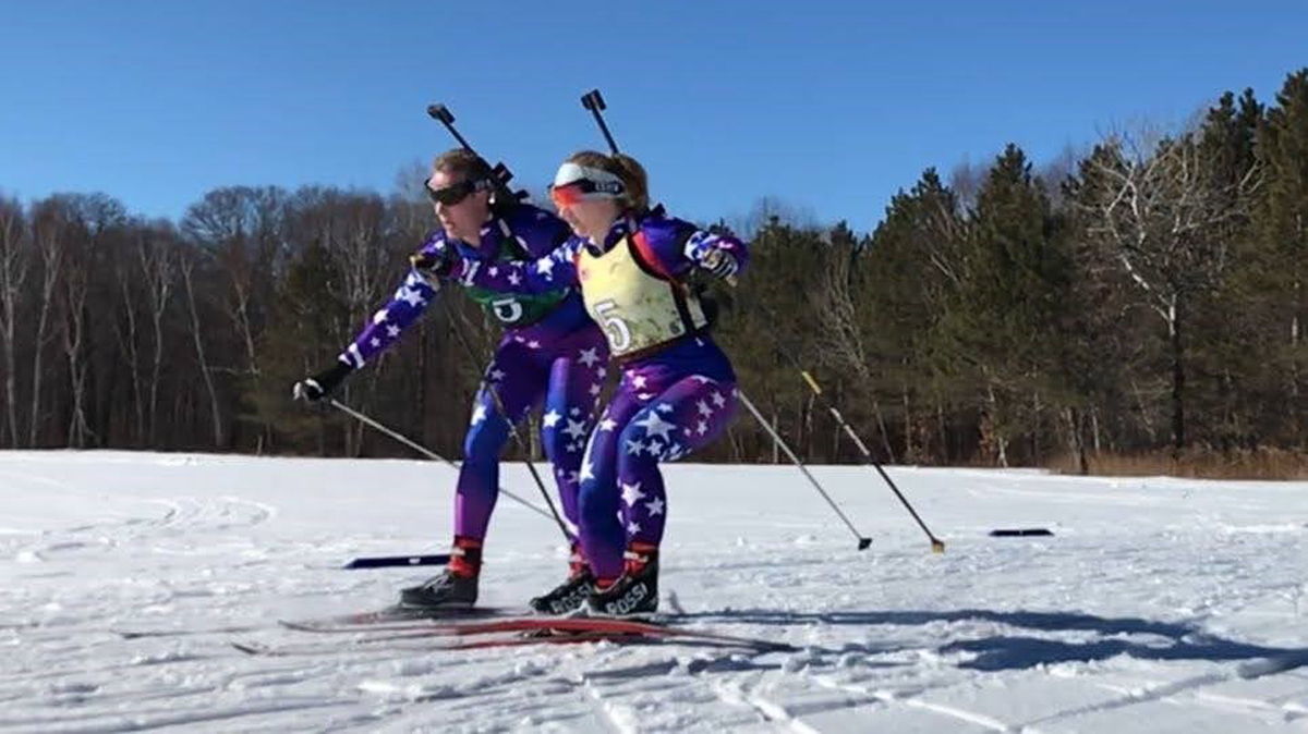 Two female biathlonm members skiing downhill