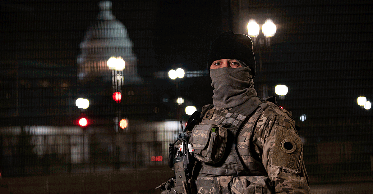 Soldier guarding capital area at night with Capitol in background.