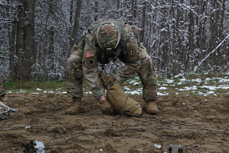 Soldier in snowy clearing bending down to prepare sandbag.