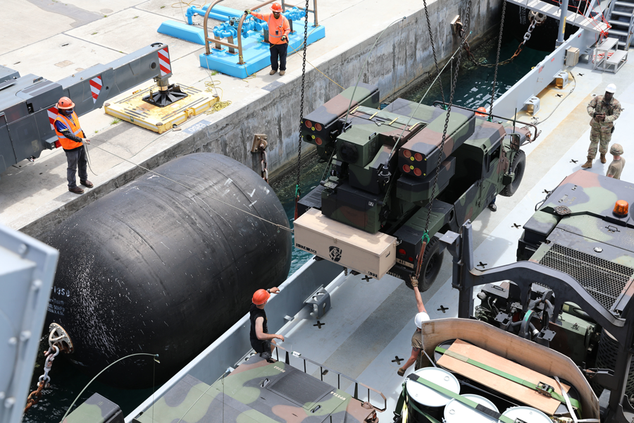 Workers load an Avenger Air Defense System onto an Army Watercraft System.