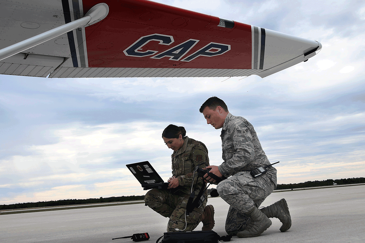 Airmen check laptop under wing of aircraft.