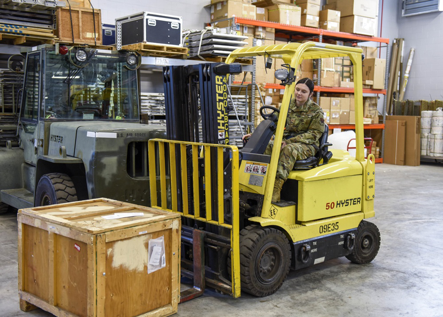 Female airman uses a forklift to move a crate in warehouse.