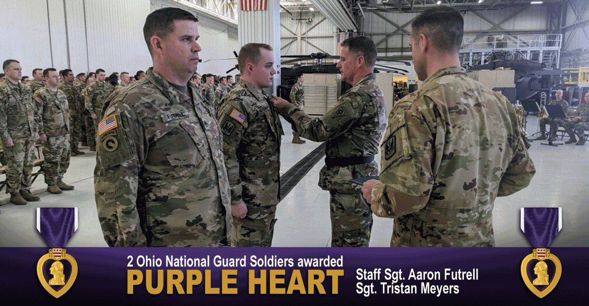 Airmen standing at attention while being pinned with purple heart at unit stands at attention observing inside hangar.