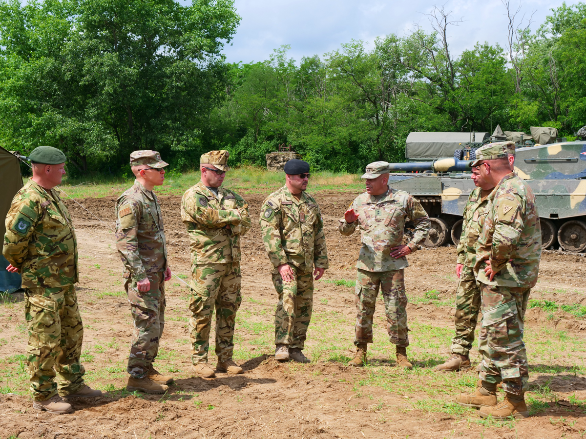 Members of the Ohio National Guard and Hungarian Defence Forces talking among tanks in field.