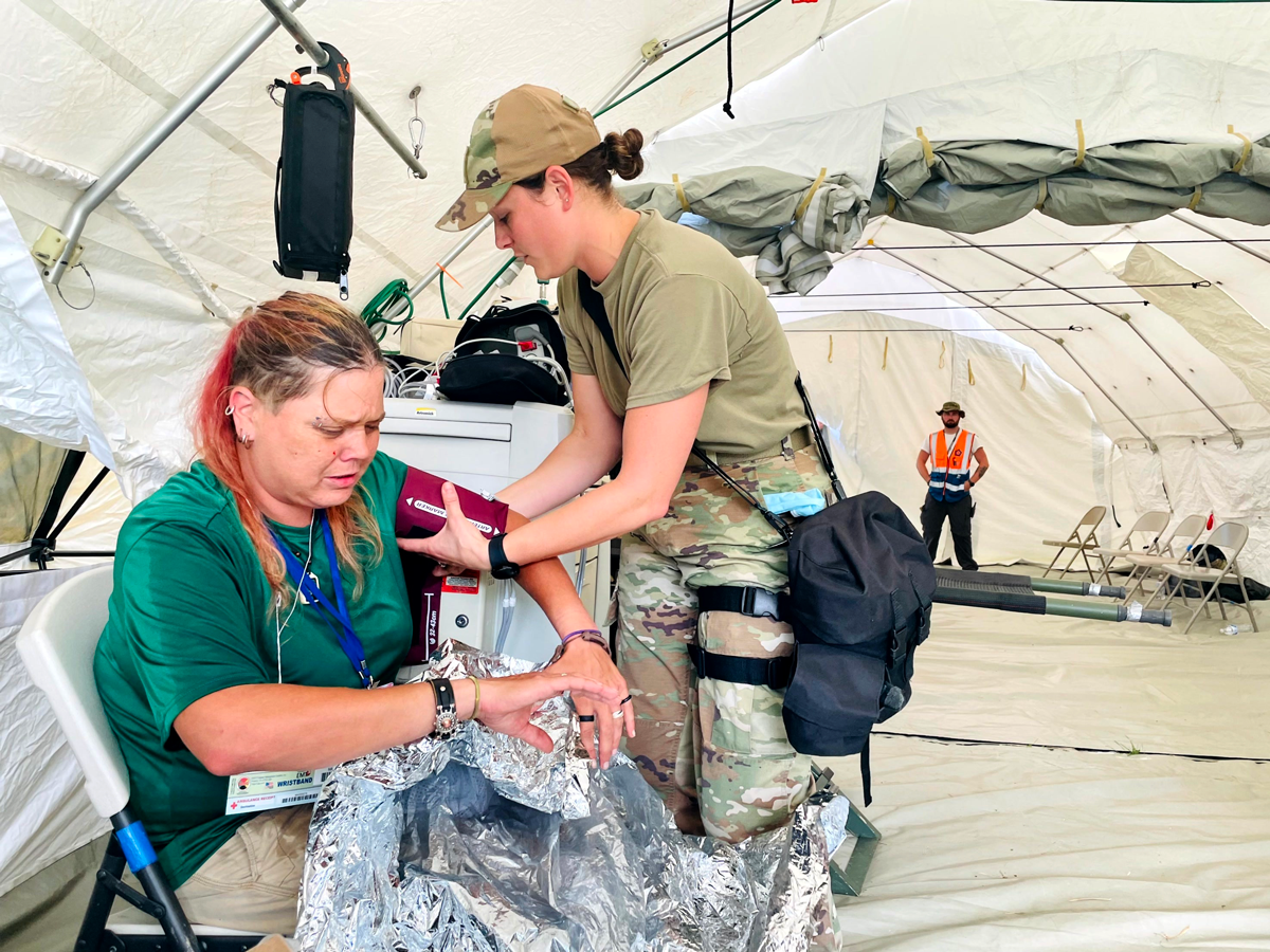  Female Guard member takes blood pressure of woman in tent area.