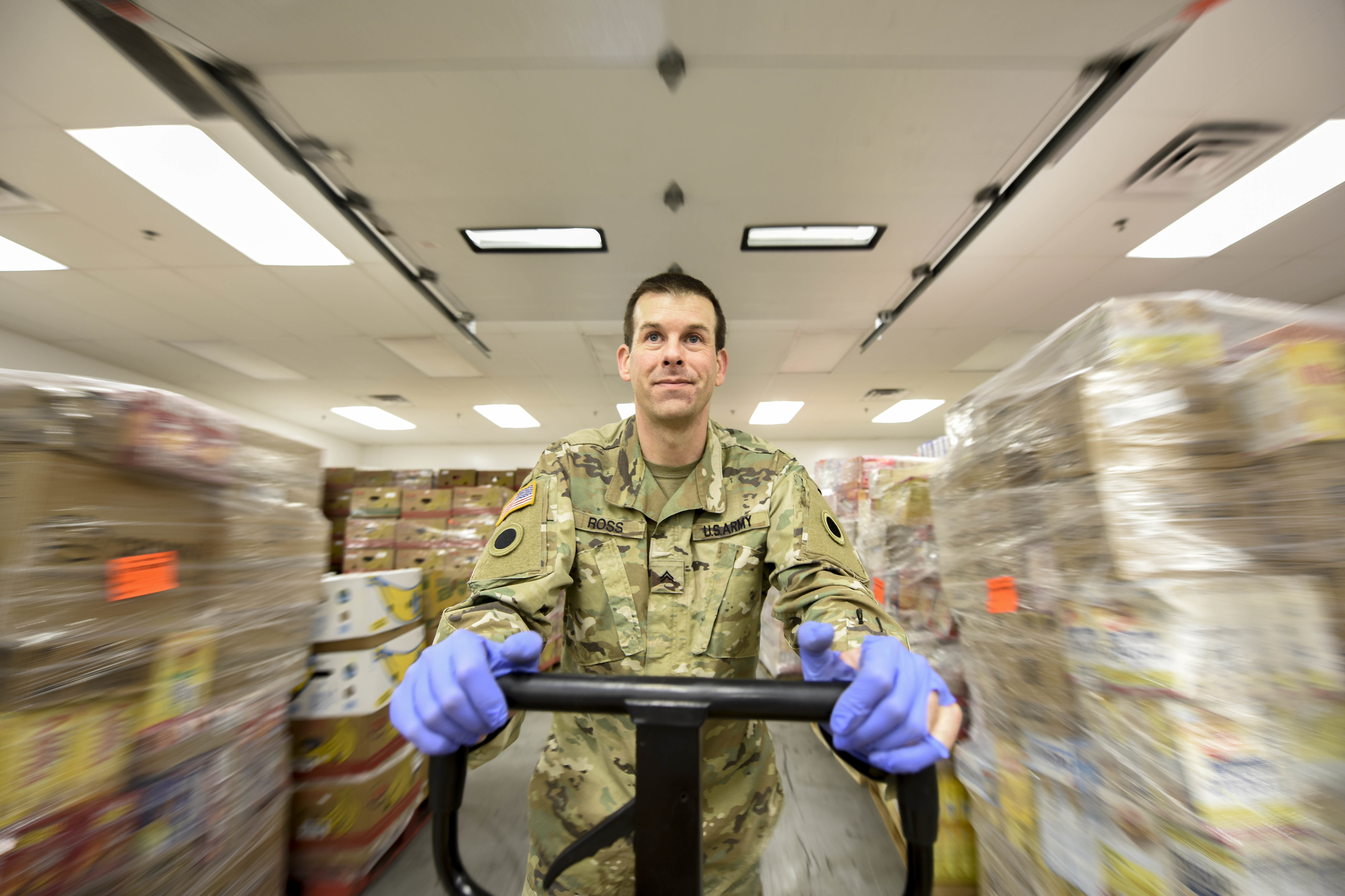 Soldier pushes hand cart through warehouse.