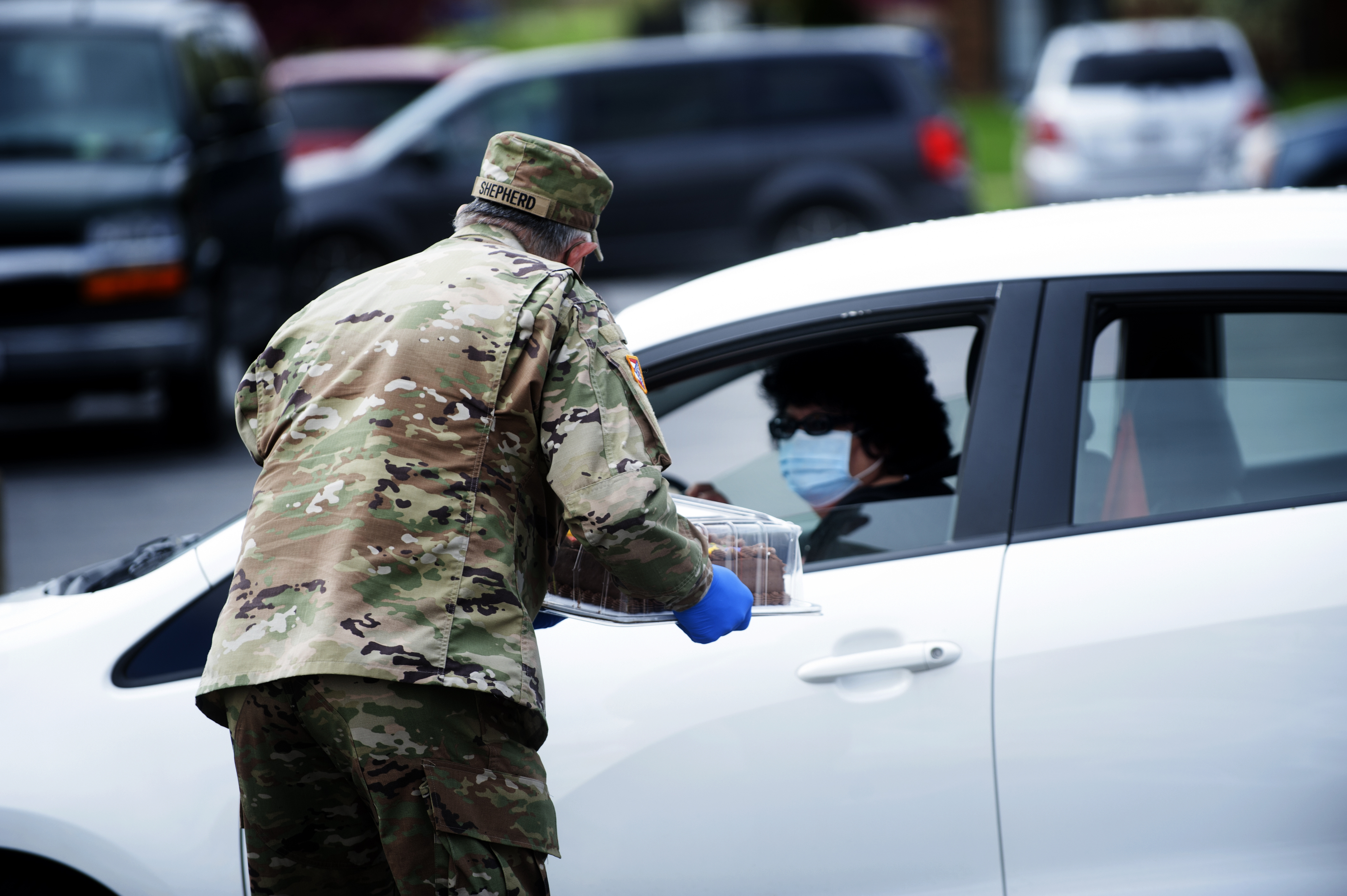 Soldier hands food to lady in car.
