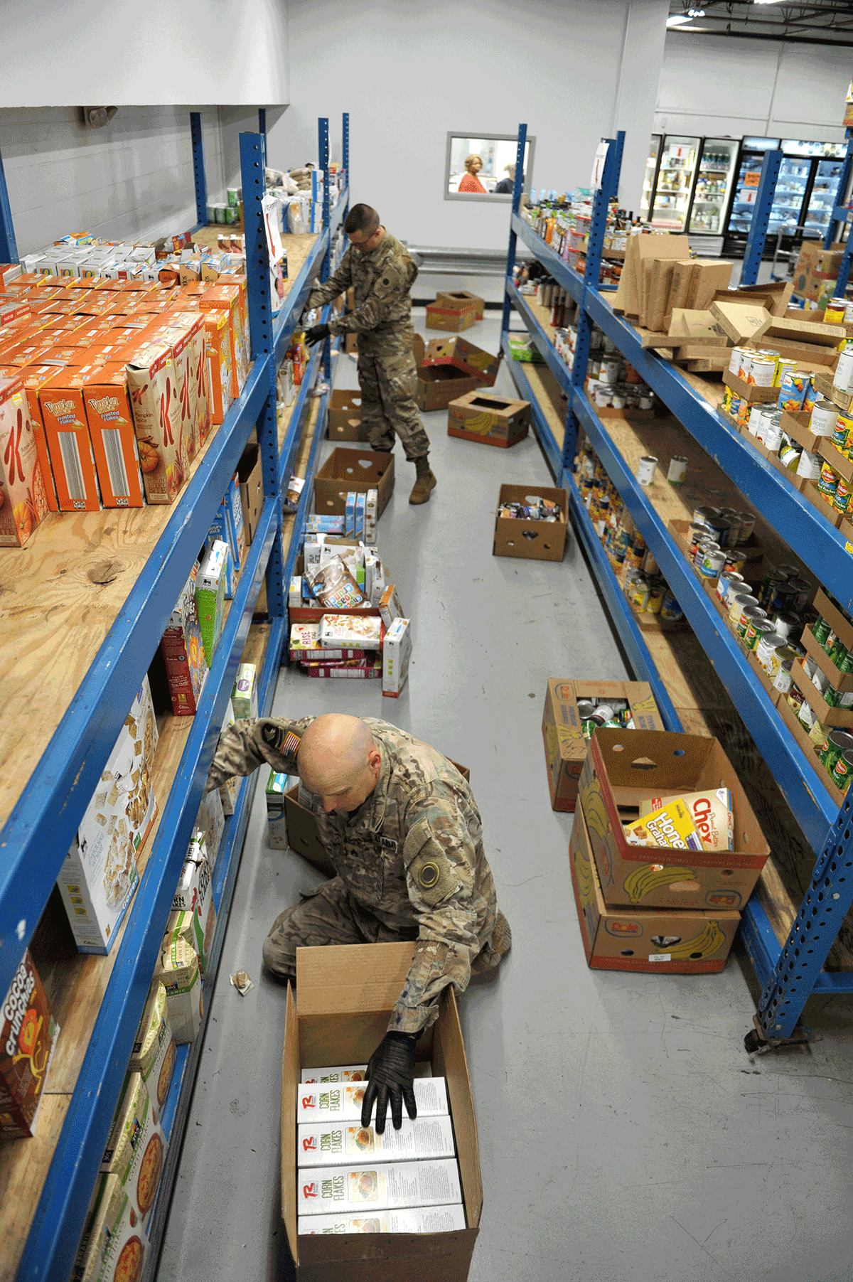Soldiers pull items from shelves in isle in warehouse.