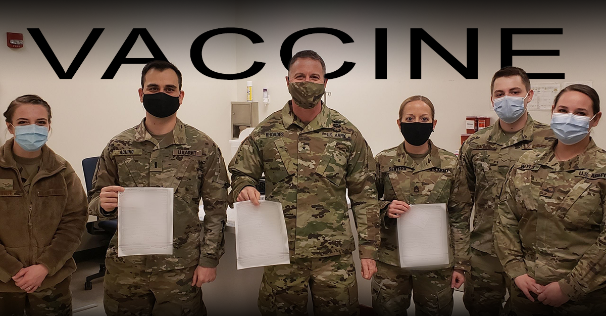 Soldiers stand in masks holding vaccine records.
