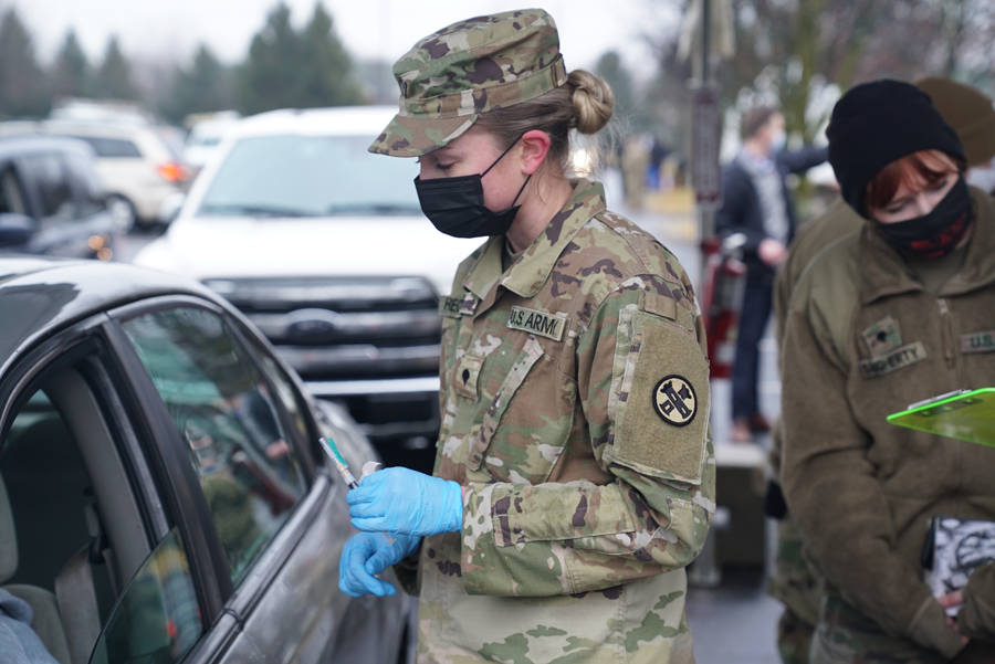 Female Guard member prepares to give vaccine to person in car.