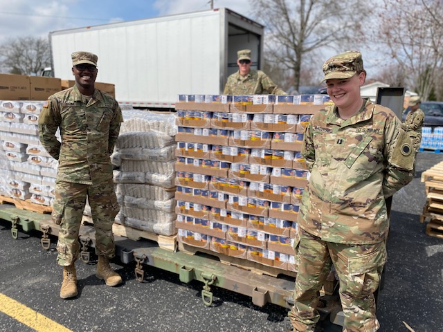 Soldiers stand by pallets of produce and canned goods.