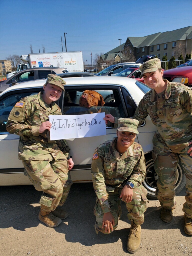 Soldiers stand outside of car in drive through with #InThisTogether signs.