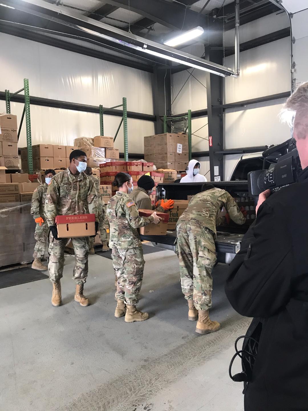 Soldiers load boxes into truck inside warehouse.