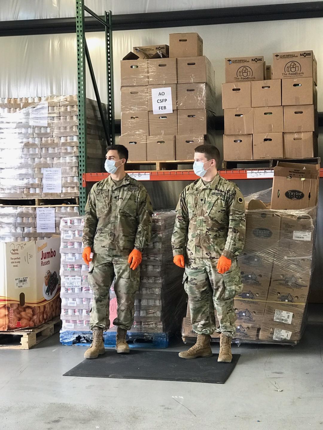 Soldiers with masks and gloves standing in front of pallets at warehouse.