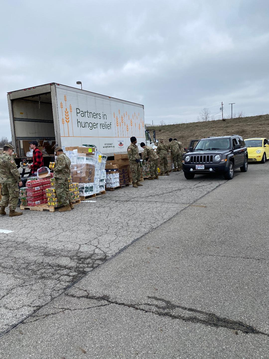 Soldiers pass out supplies from the Partners in Need semi to cars in drive through.